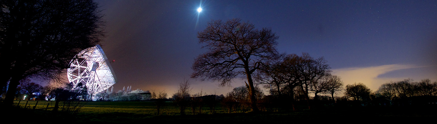 Illuminated Lovell Telescope pointing towards the moon in a night sky