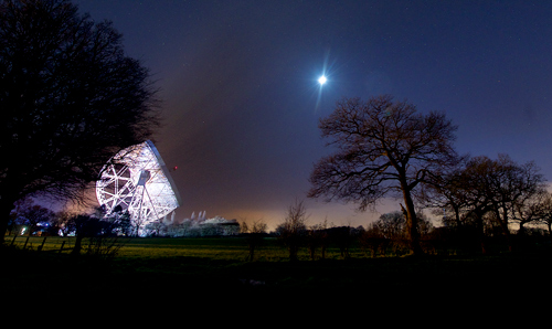 Illuminated Lovell Telescope pointing towards the moon in a night sky